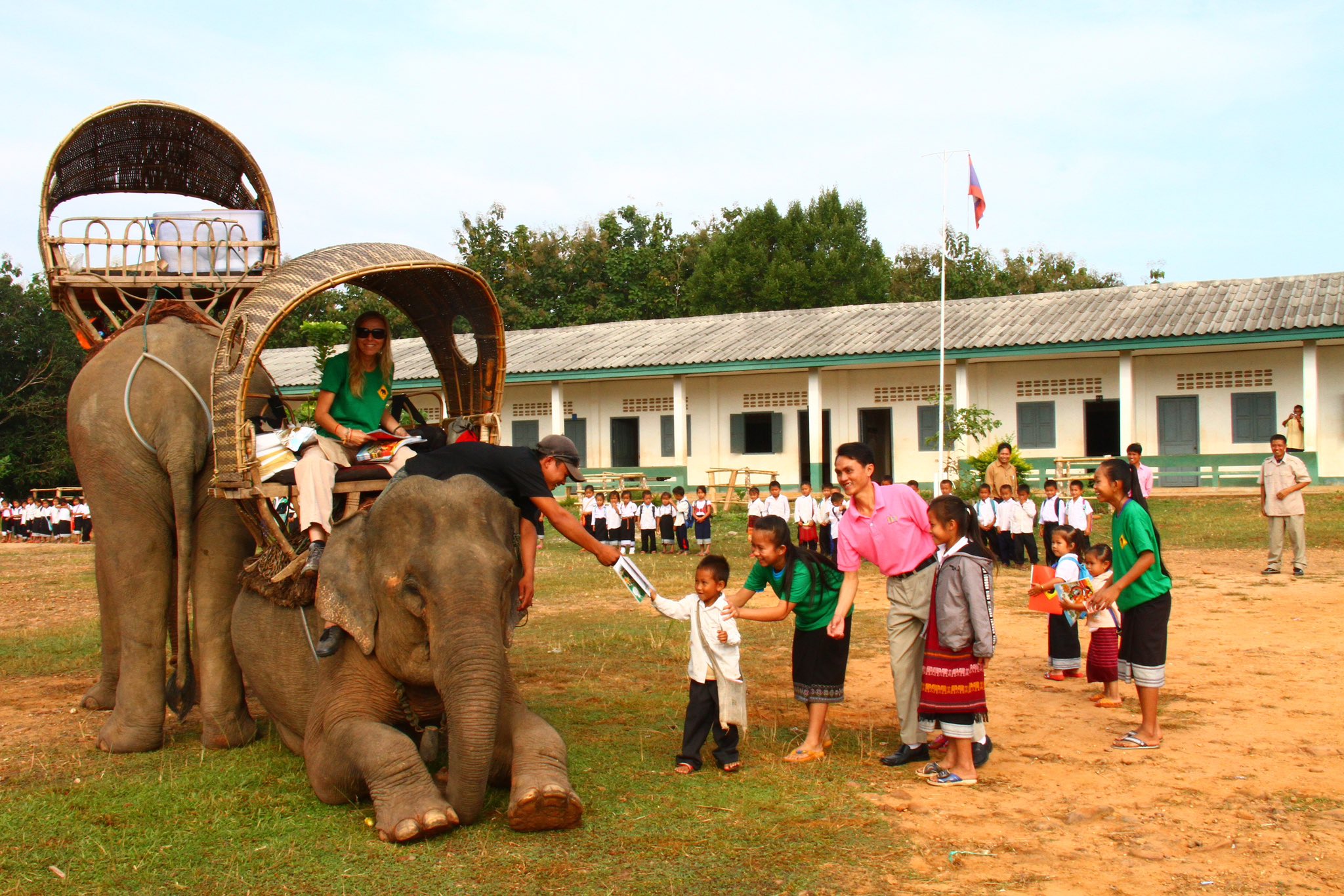 image from In Thailand and Laos, Elephant Mobile Libraries use elephants to deliver books to the remote communities inaccessible to other modes of transport. The students patiently wait in line and receive their books from the librarians seated atop the elephants.